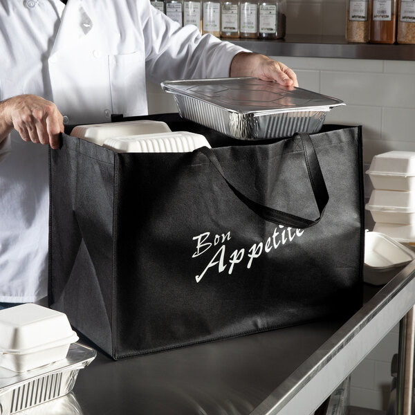 A chef in a white coat putting food into a large black non-woven bag.