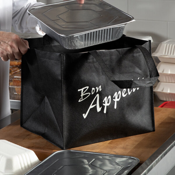 A man putting a white styrofoam container of food in a black LK Packaging reusable catering bag.