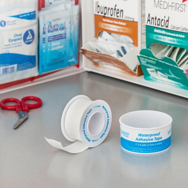 A Medi-First roll of adhesive tape next to red scissors with a white and blue label.