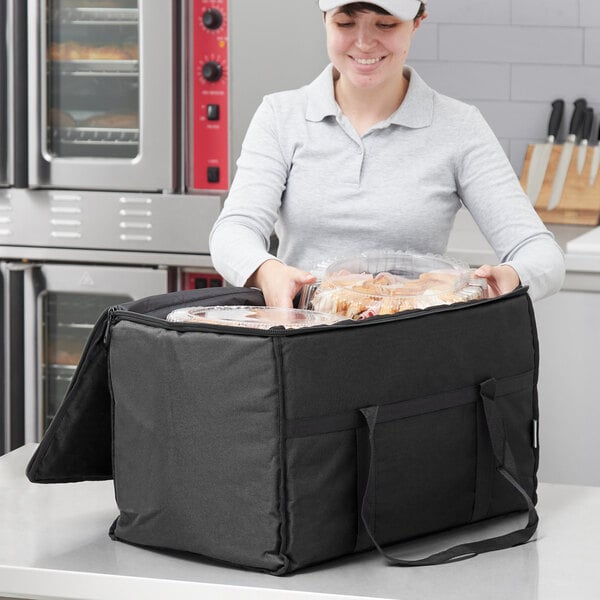 A woman holding a black Choice insulated food delivery bag with food in it.