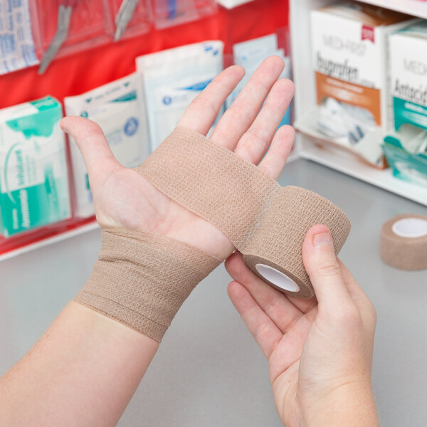 A person holding a Medi-First Rip-N-Wrap self-adhesive wrap in front of a medical cabinet.