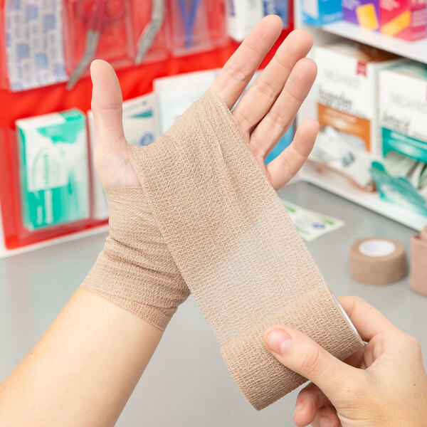 A person holding a roll of Medi-First self adhesive wrap.