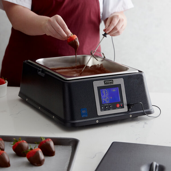 A woman pouring chocolate into a Waring chocolate melter on a counter.