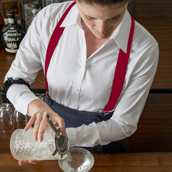 A woman using a Henry Segal red elastic clip-end suspender to pour a drink into a glass with ice.