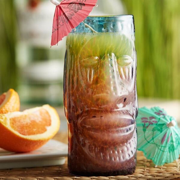 A Moai tiki glass filled with a drink and an umbrella with an orange slice on the rim.