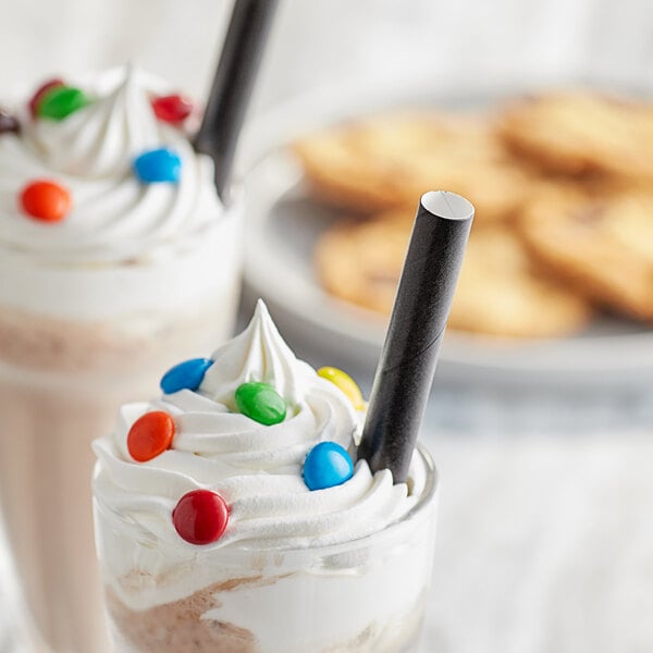 A close-up of two glasses of milkshakes with whipped cream and candy with black EcoChoice paper straws.