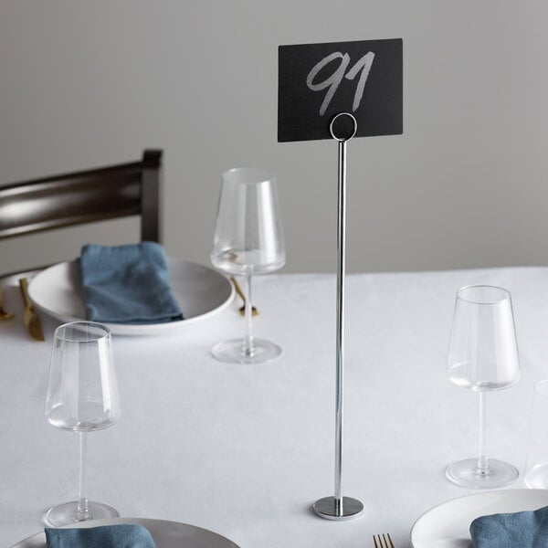 A table with a Choice 18" Chrome Menu / Card Holder on it set with place cards and silverware.