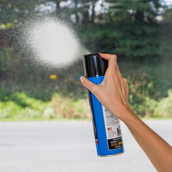 A hand holding a blue Weiman foaming glass cleaner spray can, spraying a window.