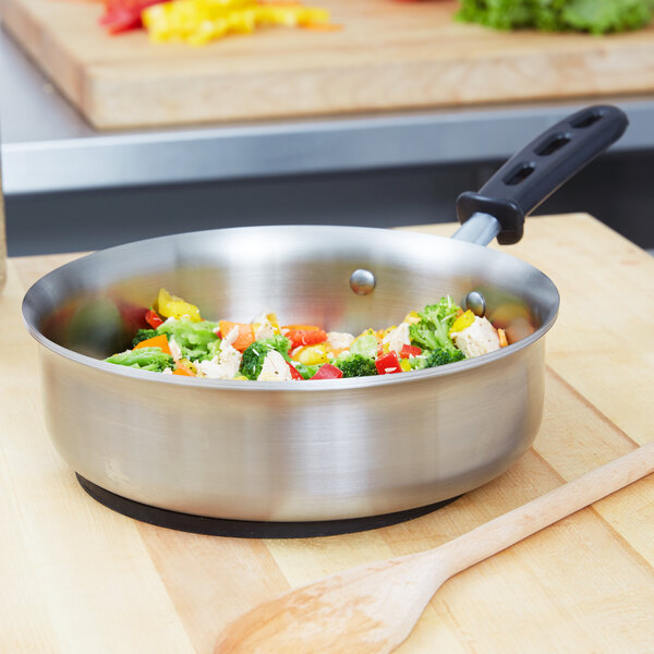 A Vollrath saute pan filled with vegetables on a table with a wooden spoon.