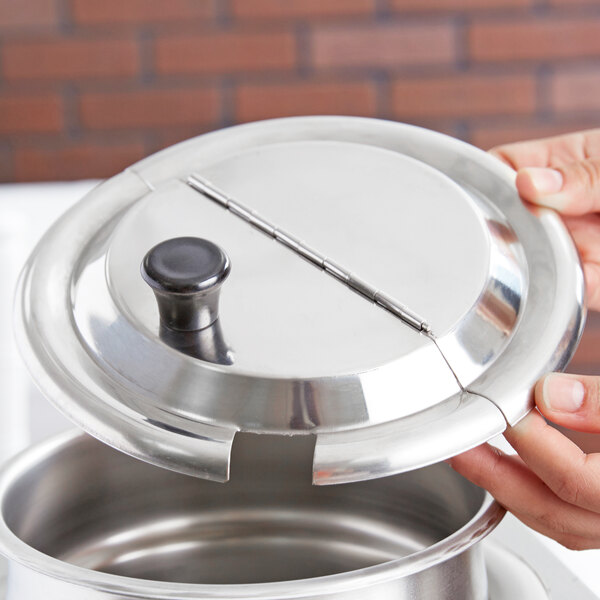 A person holding a stainless steel notched lid for a silver pot.