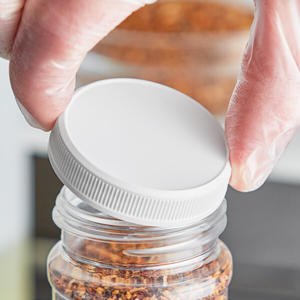 A person in gloves holding a white plastic container with a white flat plastic lid.