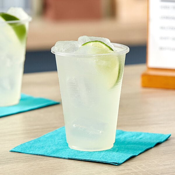 A Choice translucent plastic cup filled with ice water and a lime slice on a napkin.