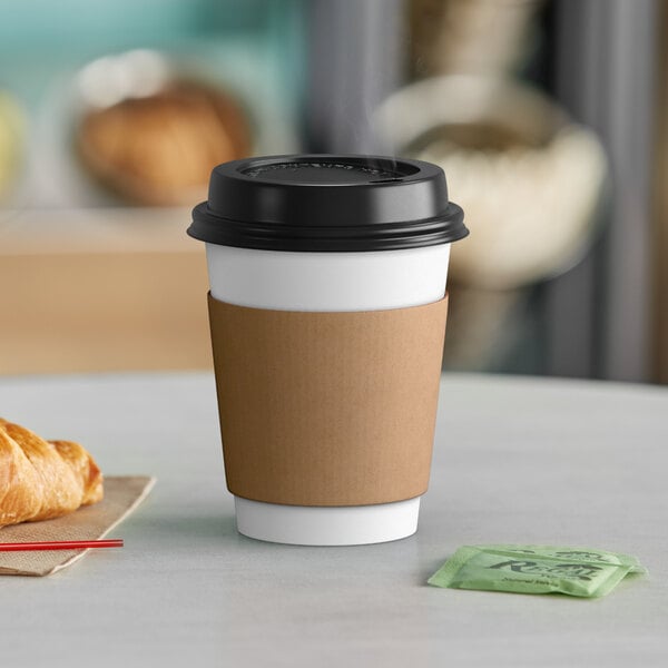 A white paper coffee cup with a black lid and a croissant on a table.