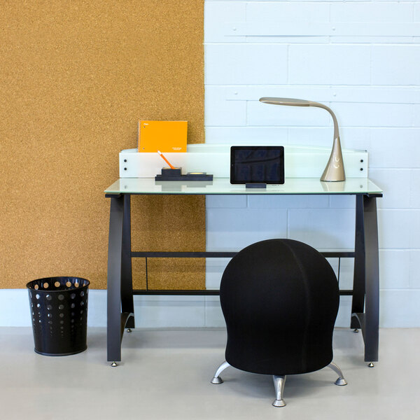 A black Safco steel round bubble wastebasket with holes in it under a desk.