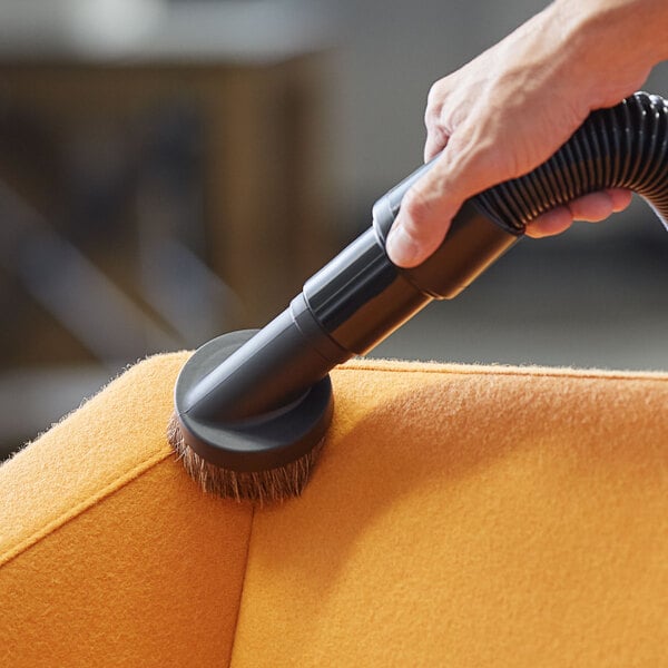 A hand using a Lavex dusting brush on a black tube attached to a vacuum cleaner.