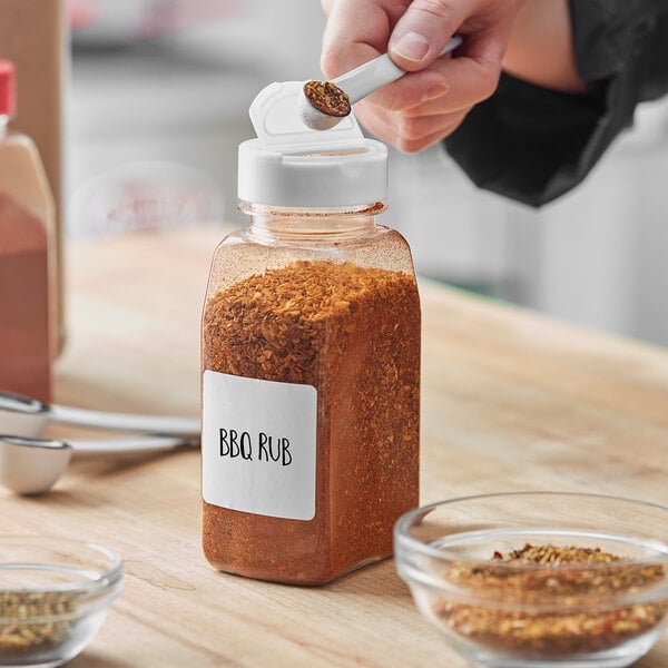 A person pouring BBQ rub into a rectangular plastic spice container with a white dual flapper lid with 3 holes.