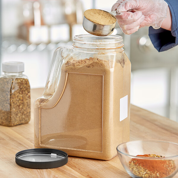 A person pouring brown powder into a rectangular plastic spice container.