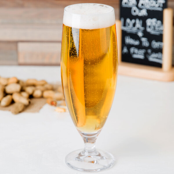 A Stolzle stemmed beer glass full of beer on a table with peanuts.
