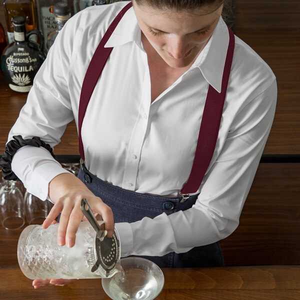 A woman using Henry Segal burgundy suspenders to pour a drink into a glass.
