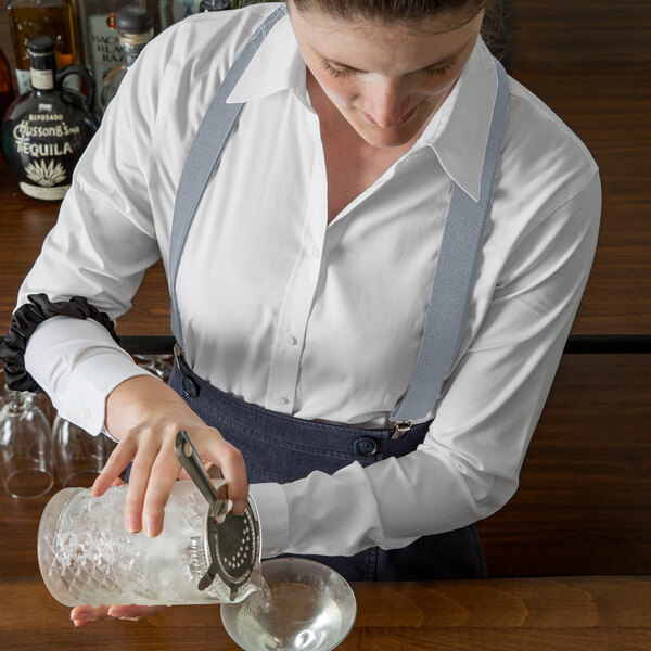 A woman using Henry Segal light grey suspenders to pour a drink into a glass.