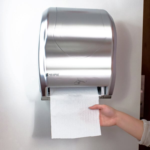 A person using a San Jamar Hybrid Summit stainless steel paper towel dispenser.