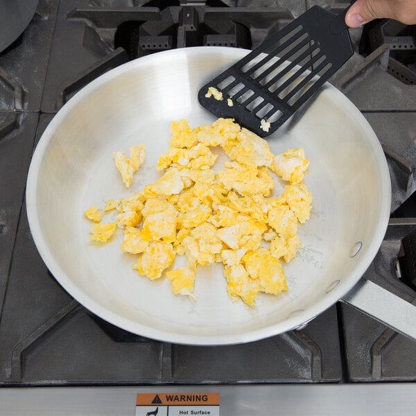 A spatula stirring scrambled eggs in a Vollrath Arkadia aluminum fry pan.