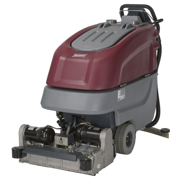A Minuteman cordless walk behind cylindrical floor scrubber with red and grey covers.