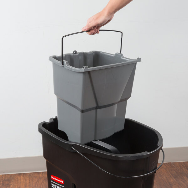 A hand using a Rubbermaid WaveBrake® mop bucket with a lid to pour dirty water into.