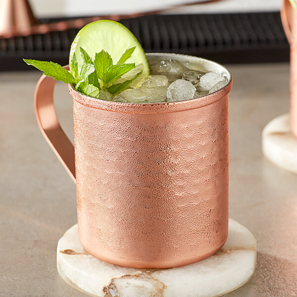 An Acopa hammered copper Moscow Mule mug filled with ice and garnished with lime and mint leaves.