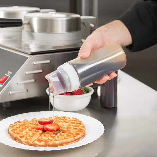A hand using a Tablecraft SelecTop squeeze bottle to pour syrup on a waffle.