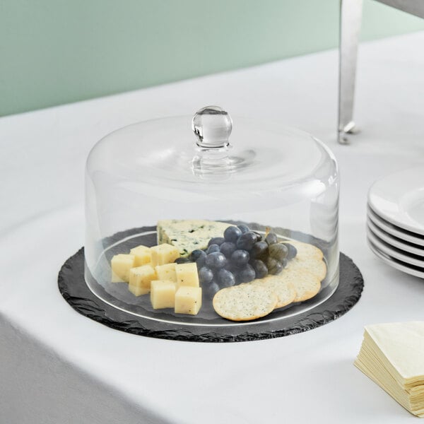 A black slate tray with a glass dome on it covering cheese and grapes.