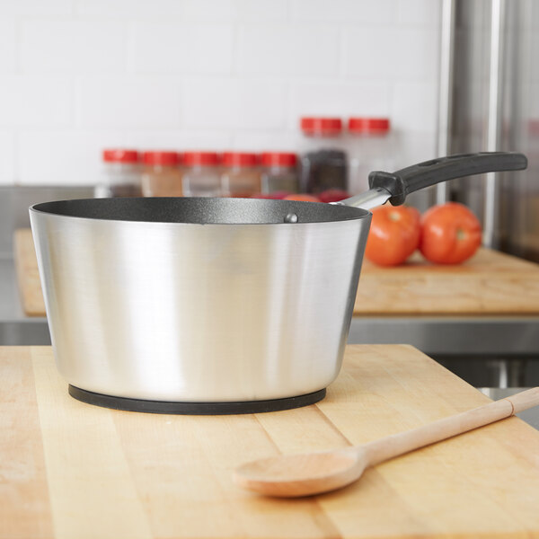 A Vollrath Wear-Ever sauce pan with a black handle on a wooden cutting board.