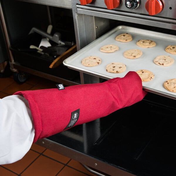 A person wearing a San Jamar Cool Touch Flame oven mitt with red sleeves putting cookies into a tray in an oven.