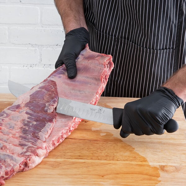 A person in black gloves using a Mercer Culinary cimeter knife to cut meat.