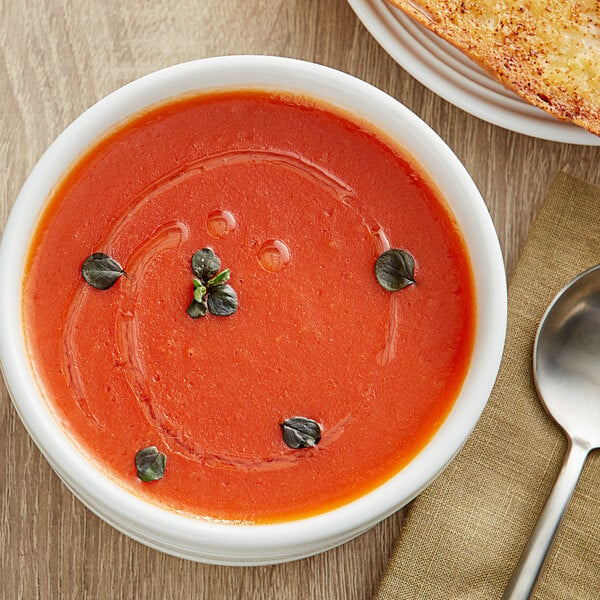 A bowl of Campbell's tomato soup with a spoon and a plate of bread.