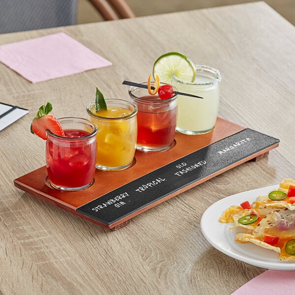 An Acopa flight tray with rounded tasting glasses filled with drinks on a table.