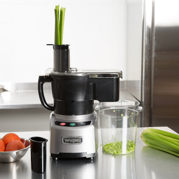 A Waring food processor on a counter with a bowl of tomatoes and a container of green onions.