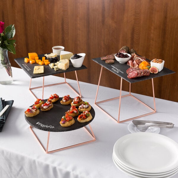 An Acopa Slate Rose Gold Wire Riser set on a table with plates of food.