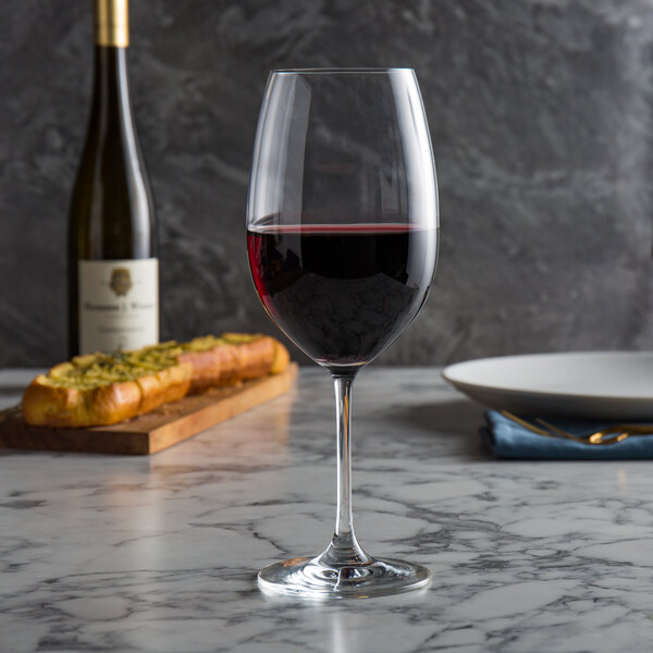 A Spiegelau Bordeaux wine glass filled with red wine on a marble table.