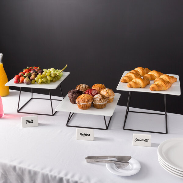 Acopa black wire risers on a table with plates of food and drinks.