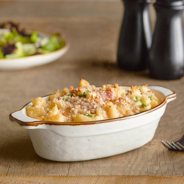 An Acopa vanilla bean stoneware oval casserole dish filled with macaroni and cheese on a table.