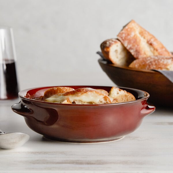 An Acopa Keystone stoneware onion soup crock filled with French onion soup and topped with melted cheese, next to a bowl of bread.