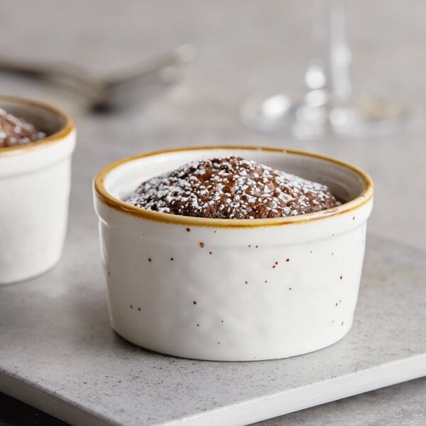 Two Acopa vanilla bean stoneware ramekins filled with chocolate pudding and powdered sugar on a white table.