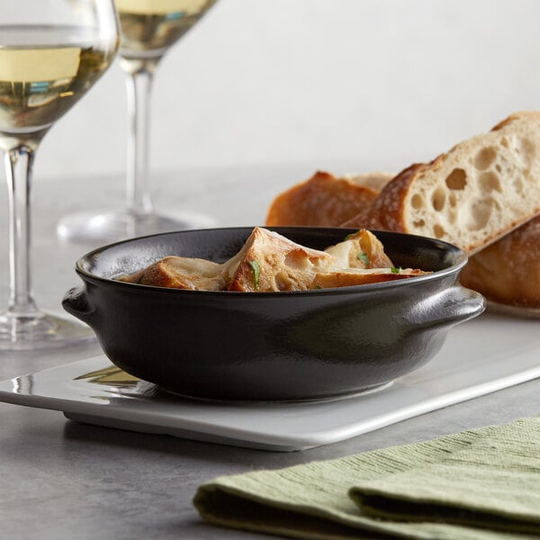 A close-up of Acopa Keystone stoneware onion soup in a bowl on a plate next to wine glasses.