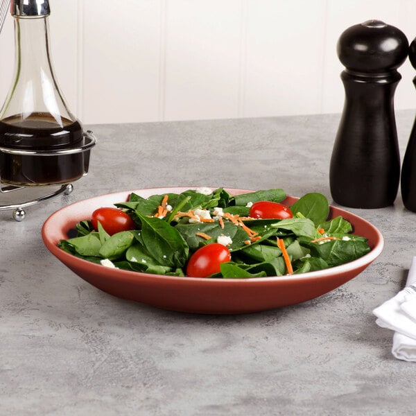 A Libbey Driftstone clay porcelain coupe bowl filled with spinach salad on a table with a pepper mill and a bottle of dark liquid.