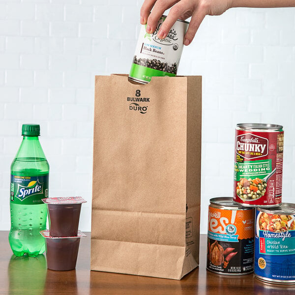 A hand putting a can of beans into a Duro brown paper bag.