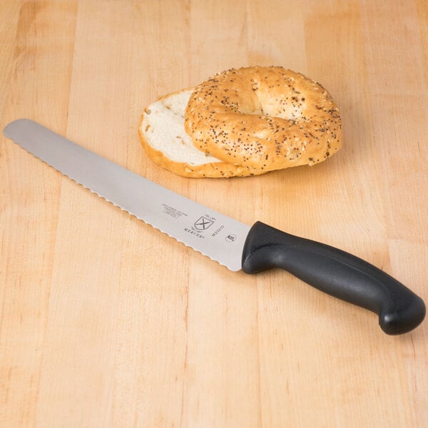 A Mercer Culinary Millennia bread knife next to a bagel on a table.