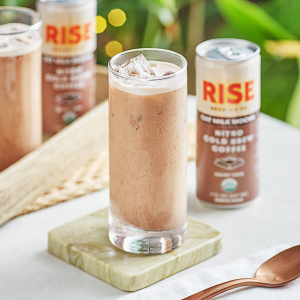 A glass of Rise Brewing Co. Organic Oat Milk Mocha Nitro Cold Brew Coffee with ice and a spoon on a wooden table.