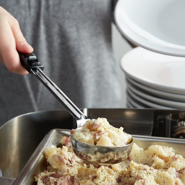 A hand using a Vollrath Black Solid Round Stainless Steel Spoodle to serve mashed potatoes.