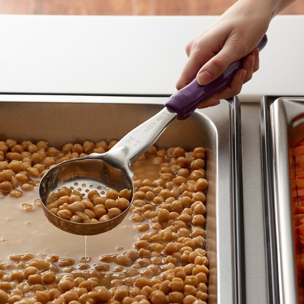 A person using a Vollrath purple perforated round Spoodle to serve food